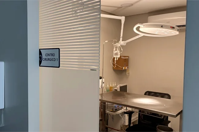 Porta do Centro Cirúrgico 1, com placa de identificação, mesa cirúrgica de inox e foco cirúrgico acima