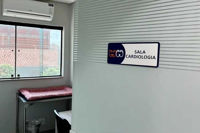 Sala de cardiologia, com placa de identificação na parede e bancada de exame junto à janela